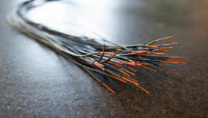 Close-up of a bundle of cut thin wires with red connections sticking out of them against a blurred electronic panel. The concept of electrical appliances in production and factory